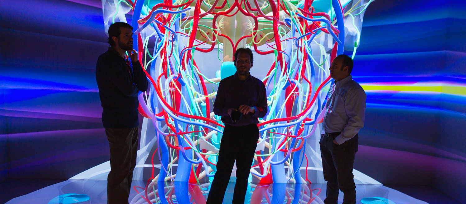 Viz Lab Leadership poses in front of image of head and neck vasculature in the Cave